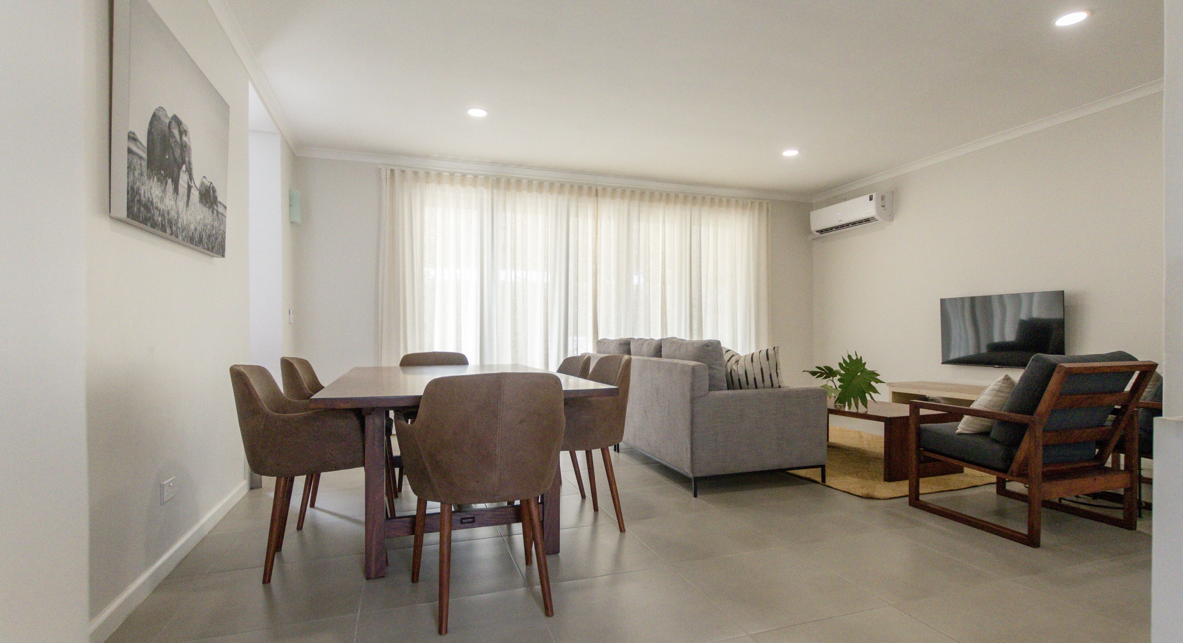 Una sala de estar moderna con comedor, un sofá, un televisor y una planta.