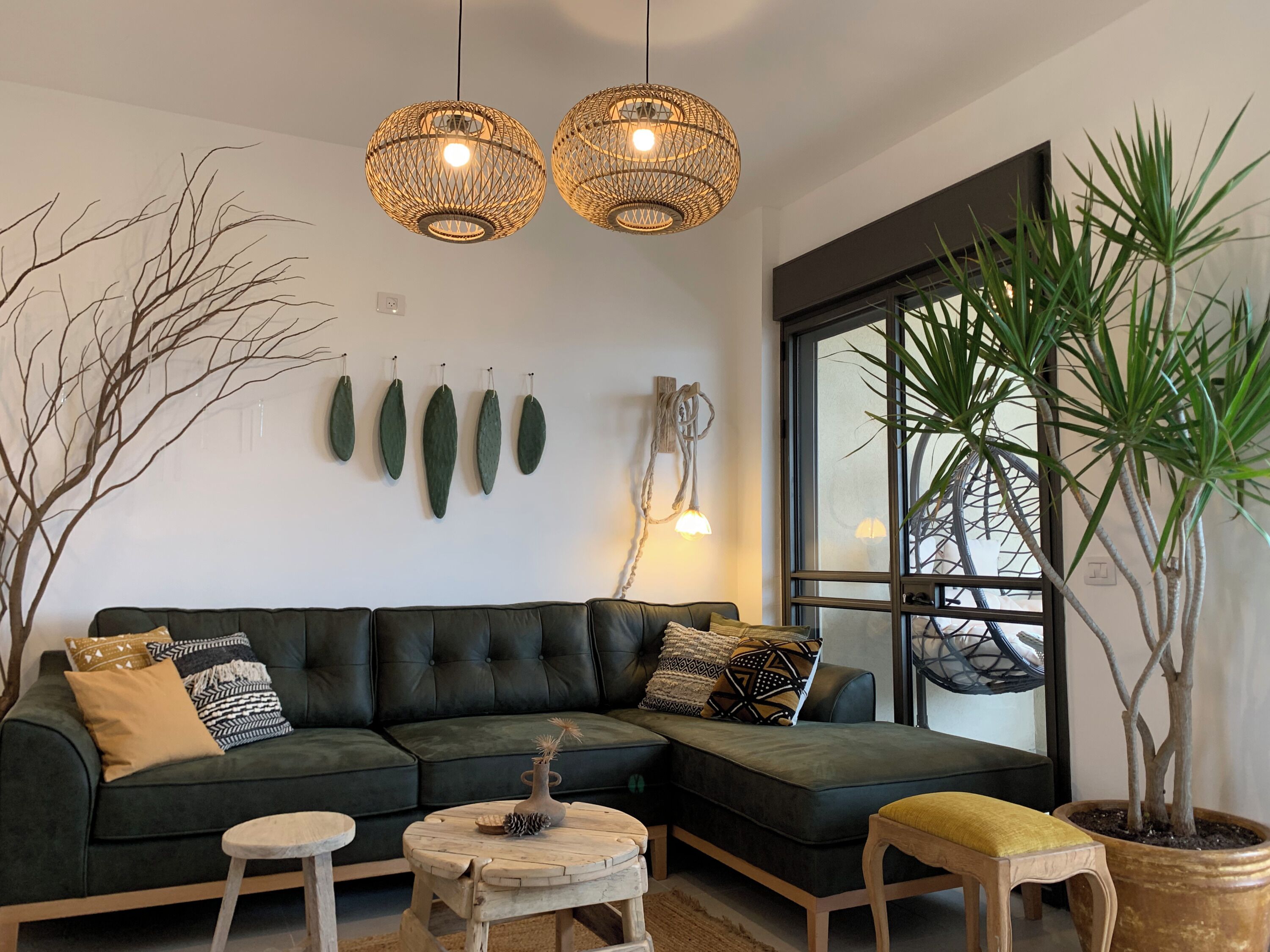 A modern living room with a sectional sofa, two hanging wicker lamps, a large window, and a potted plant.
