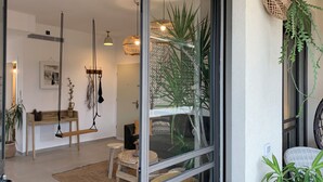 Ein modernes Interieur mit einer Glastür, die in einen Wohnbereich führt, einer Holzbank, einer hängenden Leuchte und einem Topfpflanzen.