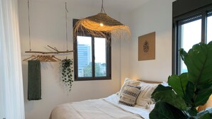 Ein Schlafzimmer mit Bett, einer hängenden Pflanze, einem Fenster und einem Wandbild.