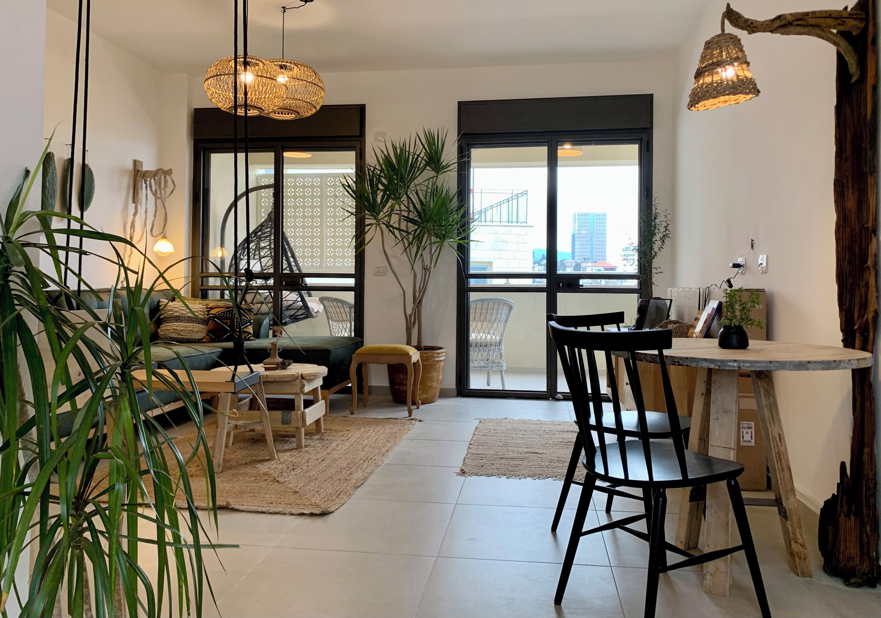 Ein modernes Wohnzimmer mit einer Couch, einem Esstisch, Stühlen und Blumentöpfen. Eine Treppe führt zu einem Balkon mit Blick auf die Stadt.