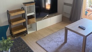 A living room with a flat-screen TV, wooden shelves, a small table, and a potted plant.