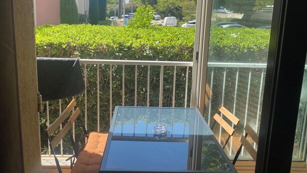 A balcony with a glass table and cushioned chairs, overlooking a residential area with buildings and greenery.