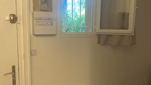 A room with a door, a thermostat, a window with a view of greenery, and a vent.