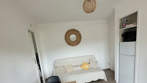 A dining area with a wooden table and chairs, a sofa with cushions, a hanging light fixture, and a refrigerator. - One-bedroom flat sleeps 4 seaside location, residence in Fabrégas, Les Sablettes (La Seyne-sur-Mer)