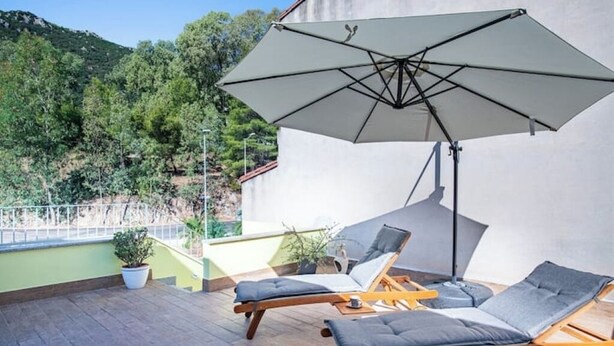 Un balcón con dos sillones de relax y una sombrilla grande, con vistas a una ladera verde.