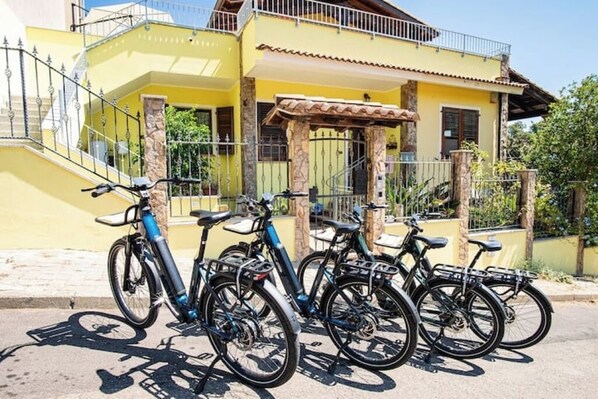 A yellow building with a staircase, a covered patio, and bicycles parked in front. - Bright and comfortable room with private bathroom (Guspini)