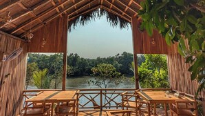 Um deck de madeira com mesas e cadeiras, com vista para um corpo d'água e vegetação.