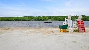 A beach with two white Adirondack chairs, a green trash bin, and a red warning sign. - Poconos Pines Escape • Sauna • Hot Tub •Playground (Pocono Lake)