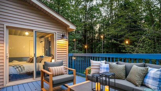 A cozy outdoor deck with a sofa, chairs, and a table, featuring a sliding glass door leading to a bedroom. - Poconos Pines Escape • Sauna • Hot Tub •Playground (Pocono Lake)