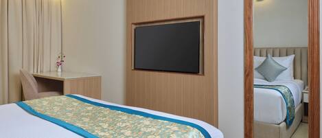 A hotel room with a bed, a desk, a chair, a TV, an air conditioner, and a mirror.
