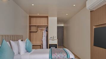 A hotel room with two beds, a wardrobe, a desk with a chair, and a television.