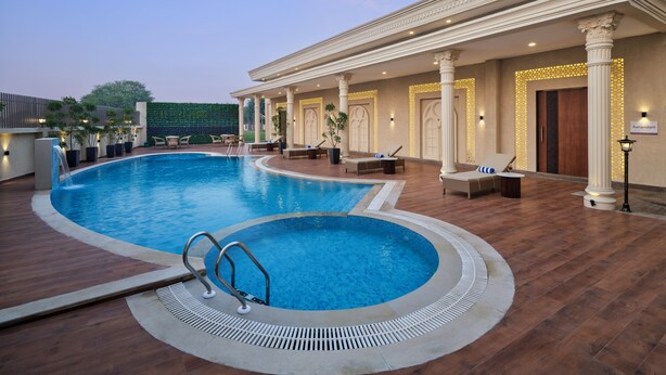 A swimming pool with a sunken area, lounge chairs, and a covered seating area with columns and lights. - Regenta Anantam Resort Khatu Shyam Ji  (Danta Ramgarh)