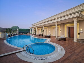 A swimming pool with a sunken area, lounge chairs, and a covered seating area with columns and lights. - Regenta Anantam Resort Khatu Shyam Ji  (Danta Ramgarh)