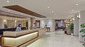 Un espace d’accueil d’hôtel comprenant un comptoir en marbre, un bureau d’accueil et un coin salon avec des chaises et une table.