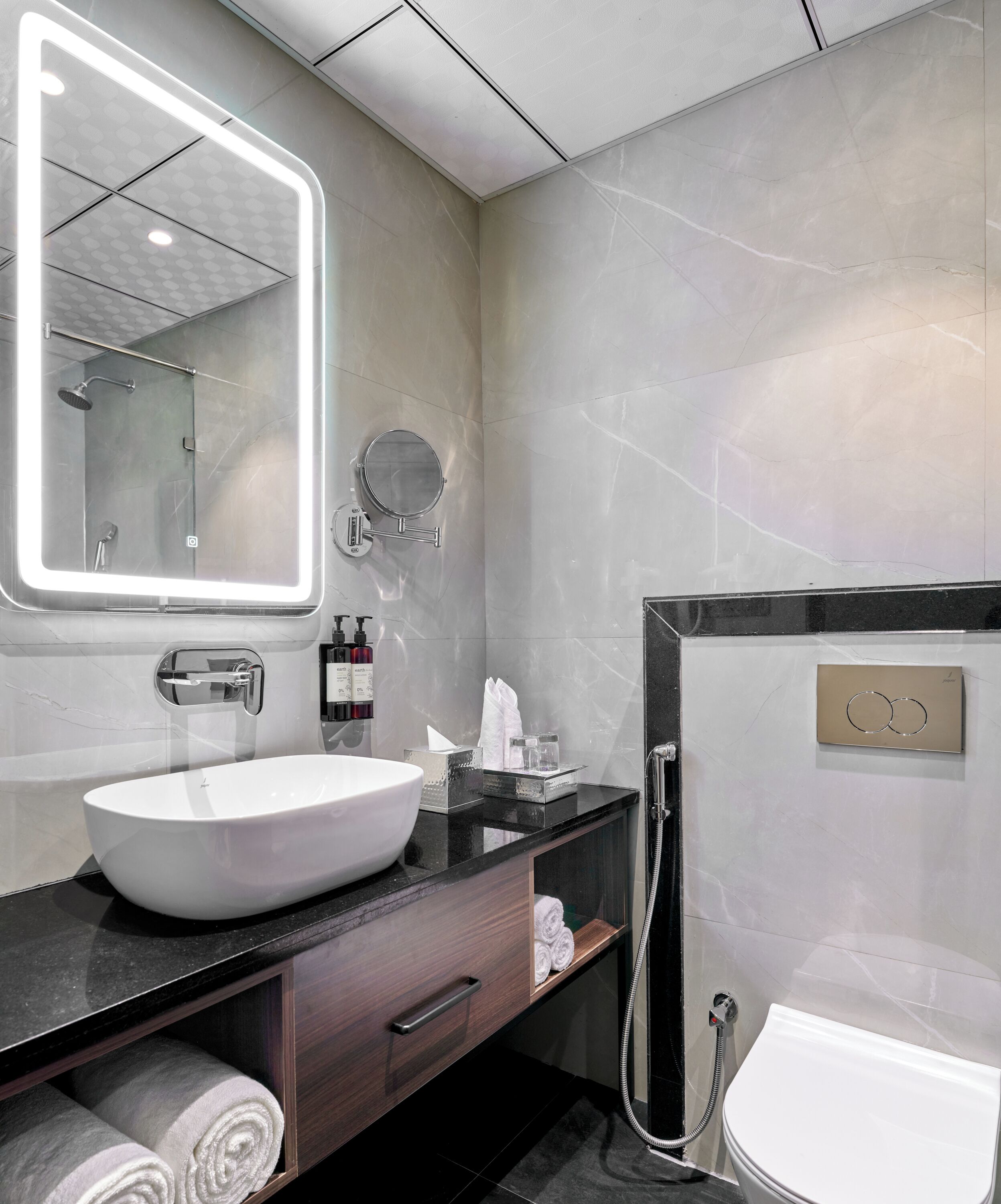 A modern bathroom with a large mirror, a white sink, a handheld shower, and a toilet.
