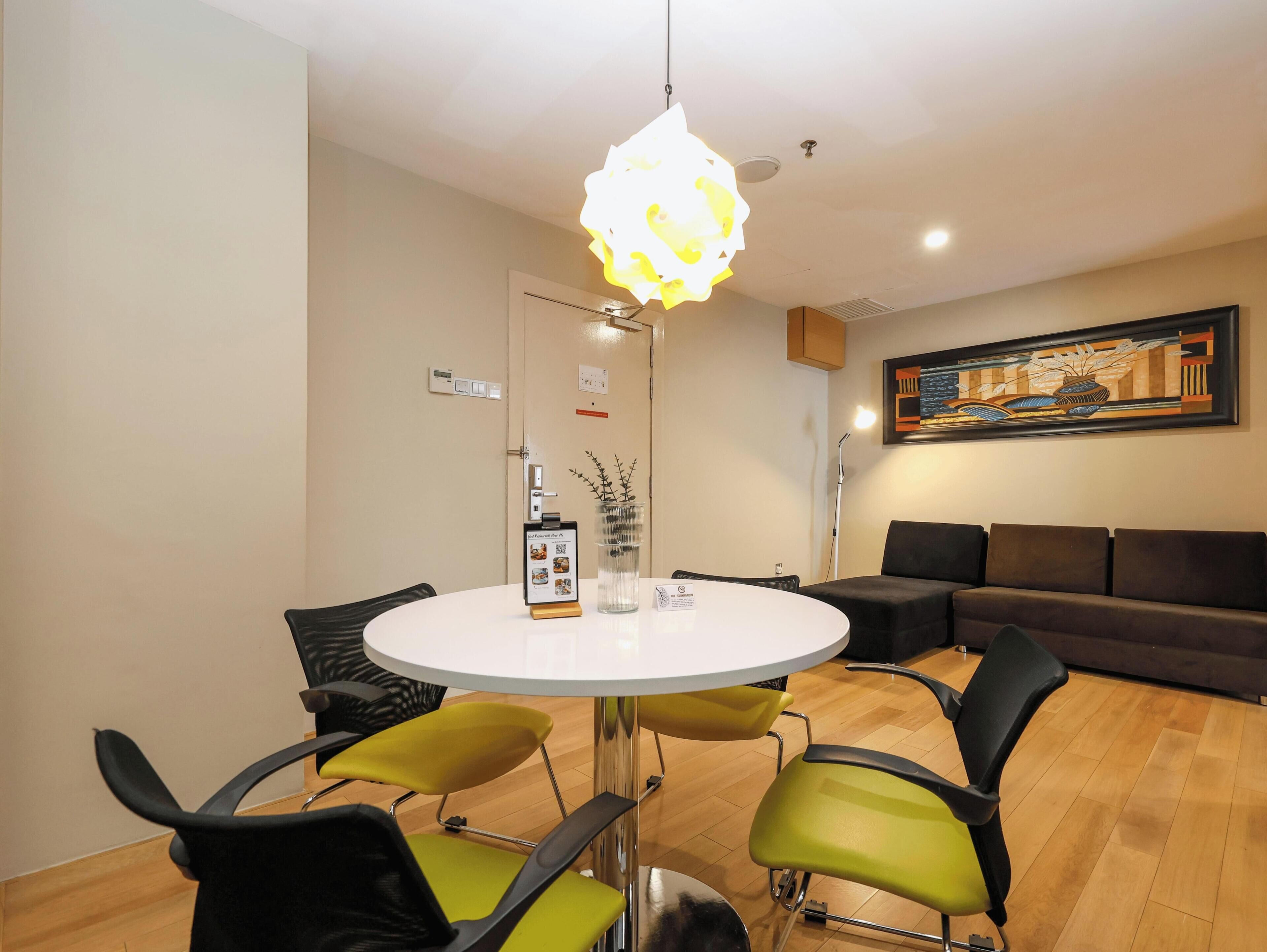 Un espace repas moderne avec une table ronde, des chaises vertes et noires, un luminaire original et un tableau accroché au mur.