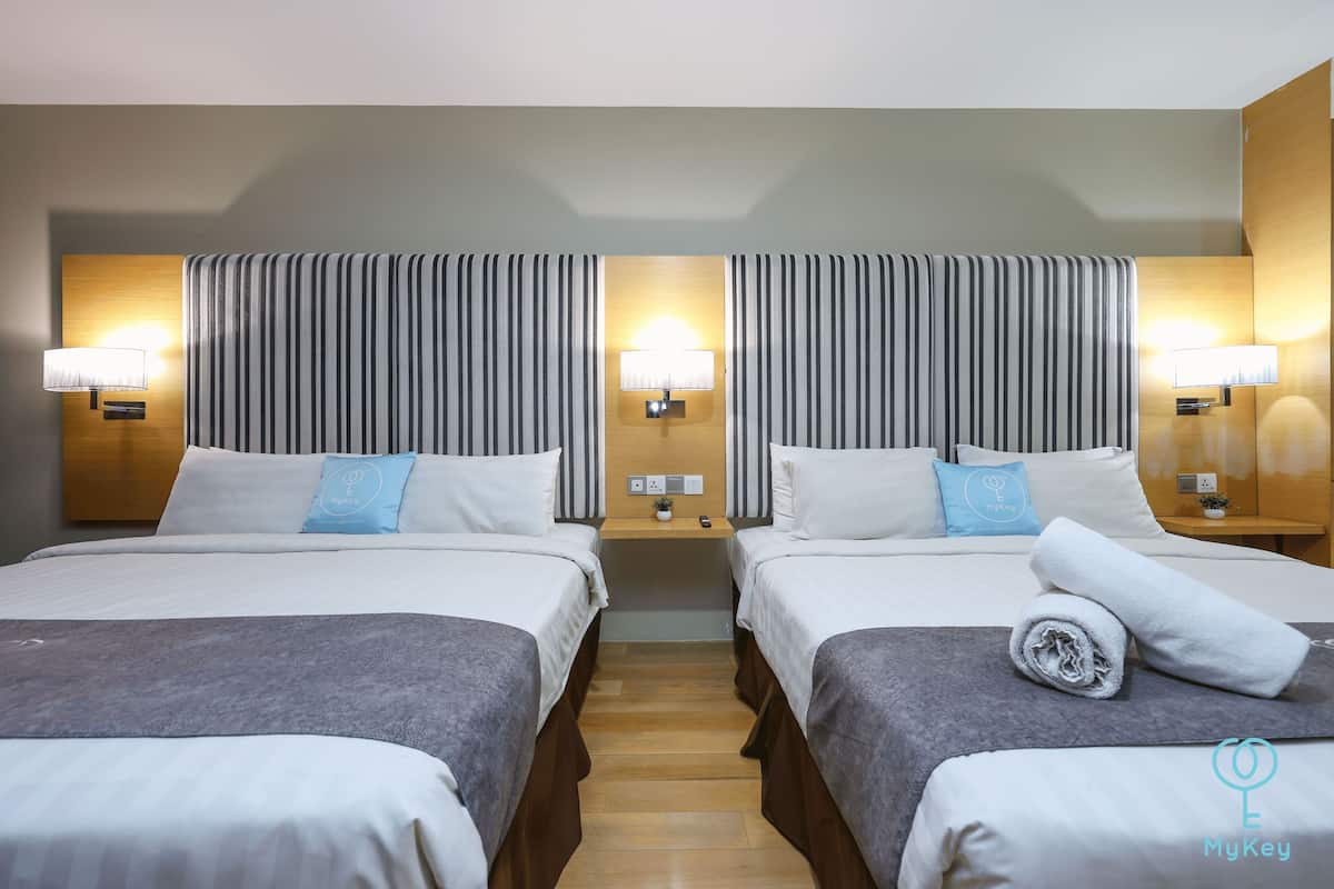 Une chambre d’hôtel avec deux lits, chacun étant équipé d’un oreiller et d’une lampe. Une petite table se trouve entre les lits, et une plante y est posée.