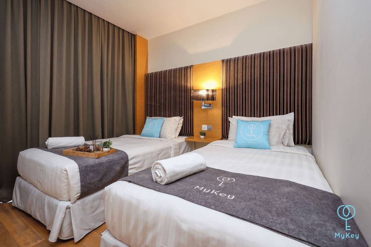 Une chambre d’hôtel avec deux lits, chacun muni d’un oreiller et d’un plateau sur lequel est posée une plante. La chambre est dotée d’une tête de lit en bois et d’une lampe fixée au mur.