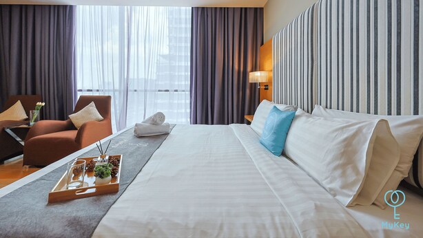 A hotel room with a large bed, a sofa, a chair, and a window with curtains. - Empire Suite Subang by MyKey (Subang Jaya)
