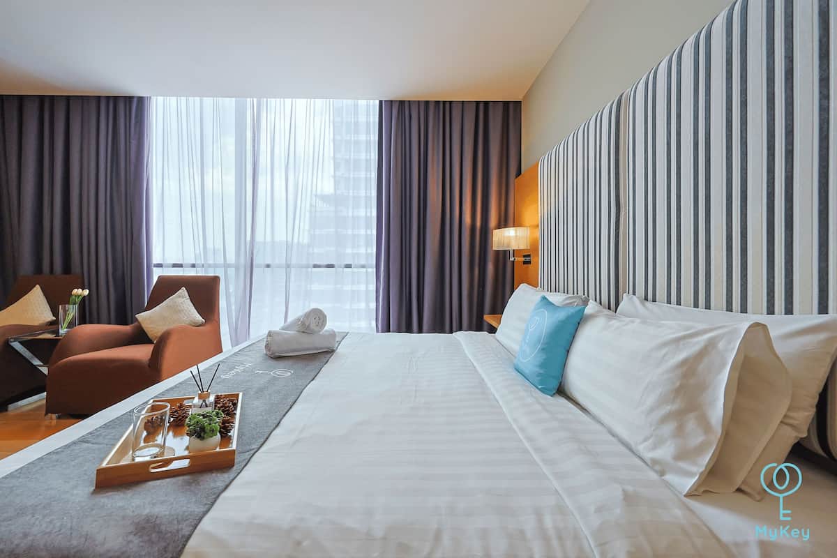 Une chambre d’hôtel avec un grand lit, un canapé, un fauteuil et une fenêtre avec des rideaux.