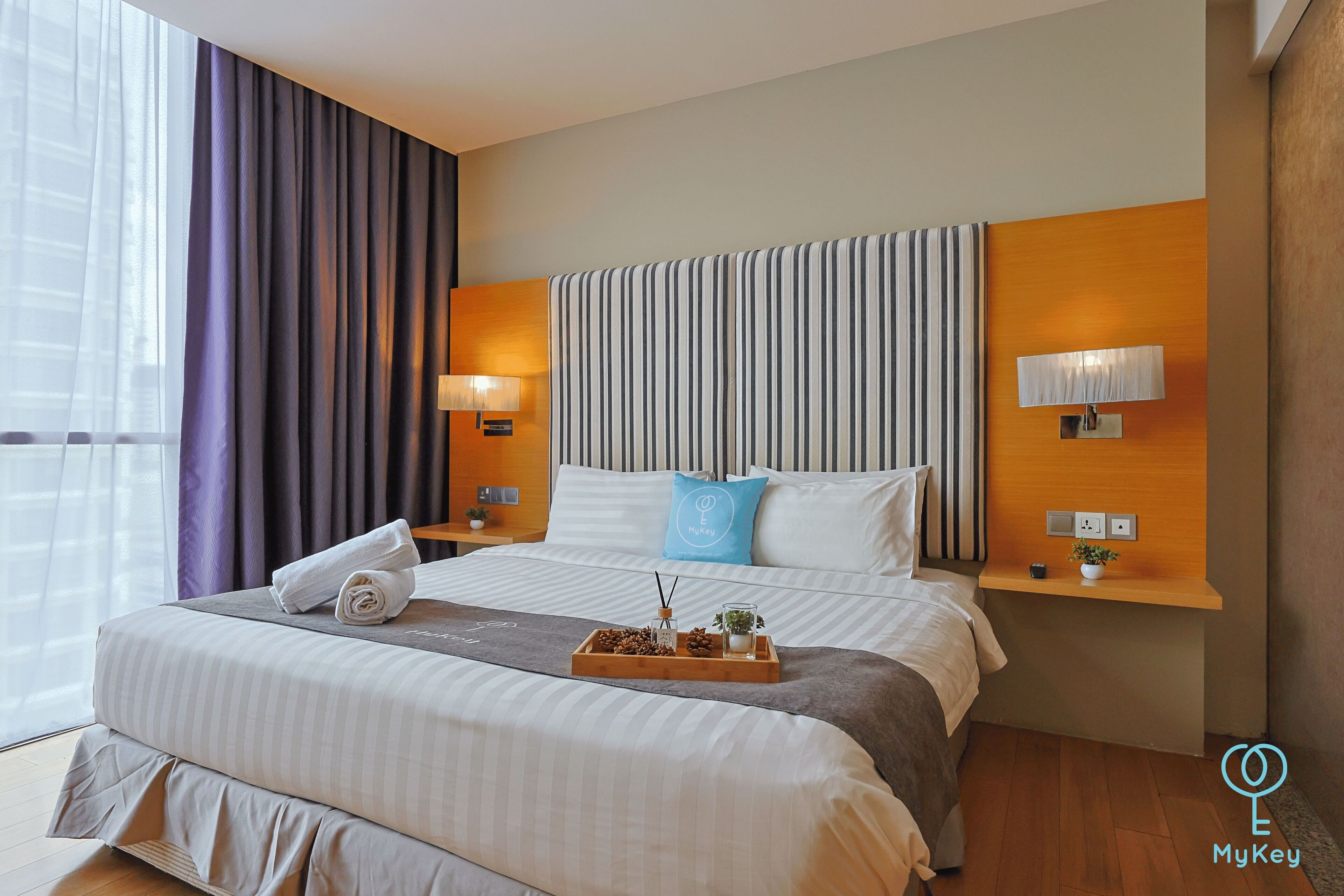 A hotel room with a large bed, two bedside tables, a headboard with vertical stripes, and a window with curtains.