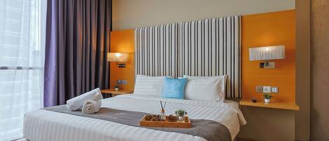 A hotel room with a large bed, two bedside tables, a headboard with vertical stripes, and a window with curtains.