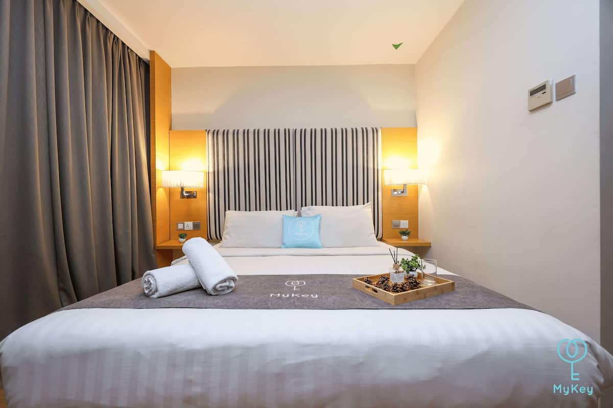 Une chambre d’hôtel avec un lit soigneusement fait, deux lampes de chevet, une tête de lit à rayures et un plateau avec une plante et des pommes de pin.