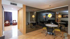 A modern hotel room with a wooden floor, a dining area with round tables and chairs, and a living area with sofas and a large mirror. - Empire Suite Subang by MyKey (Subang Jaya)
