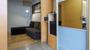 A modern room with a sectional sofa, a small desk with a computer, and a built-in wardrobe. - Empire Suite Subang by MyKey (Subang Jaya)