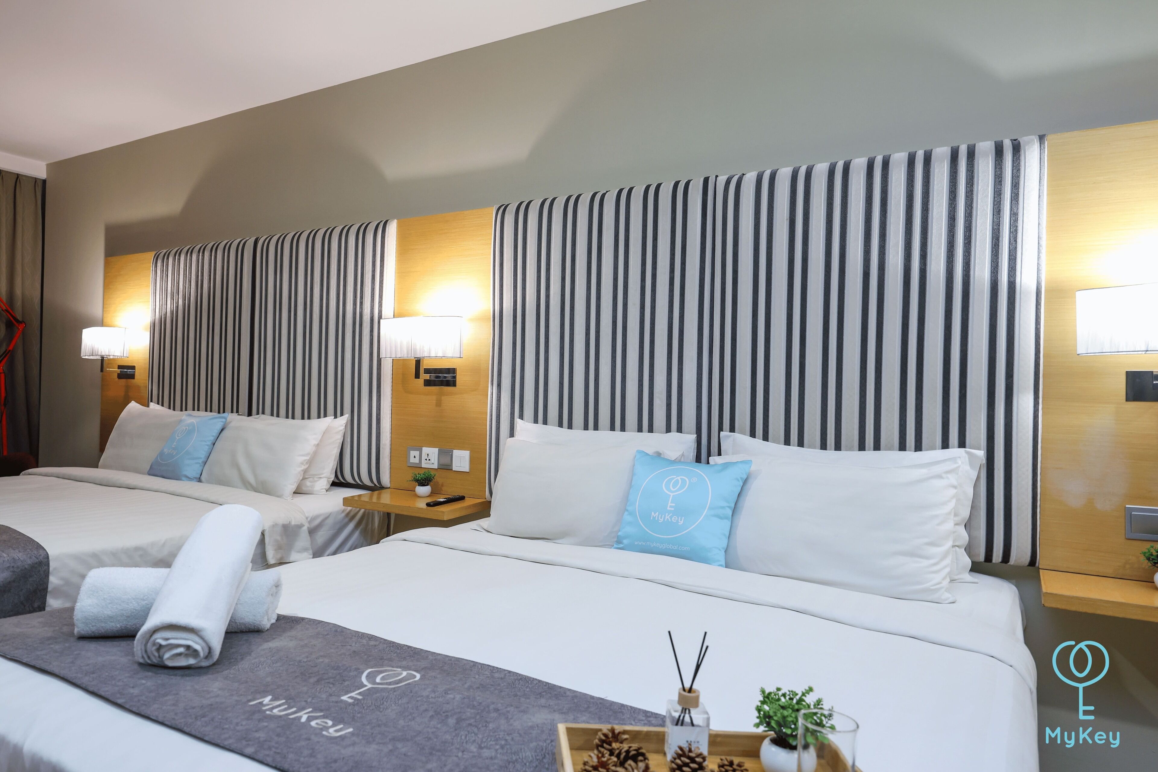 A hotel room with two beds, striped curtains, a wooden headboard, and a nightstand with a lamp.