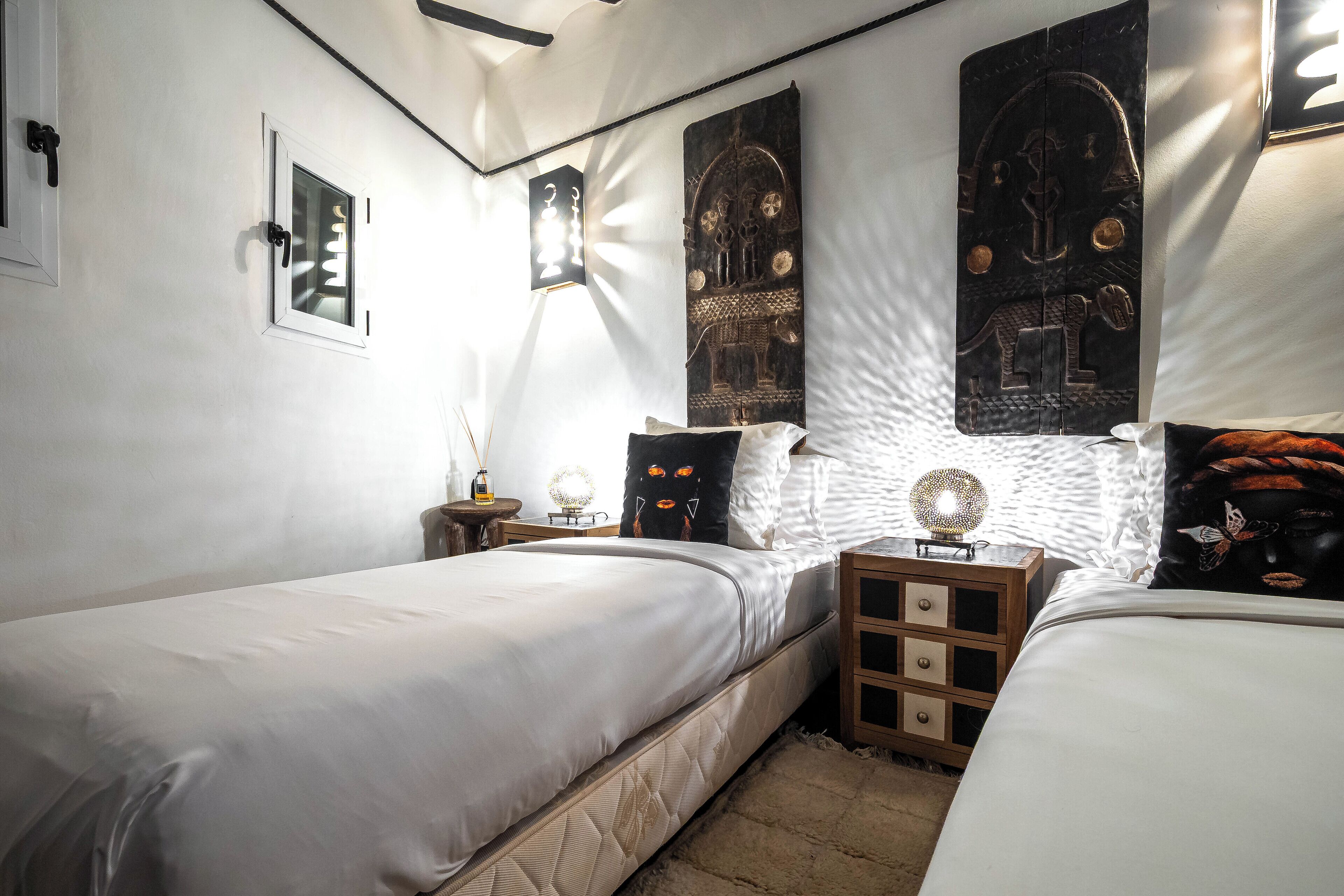 A bedroom with two beds, a nightstand, a lamp, and decorative wall art.