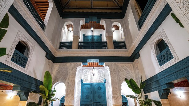 An ornate interior with a central blue door, intricate architectural details, and potted plants. - Dar Alhambra Riad Medina (Marrakech)