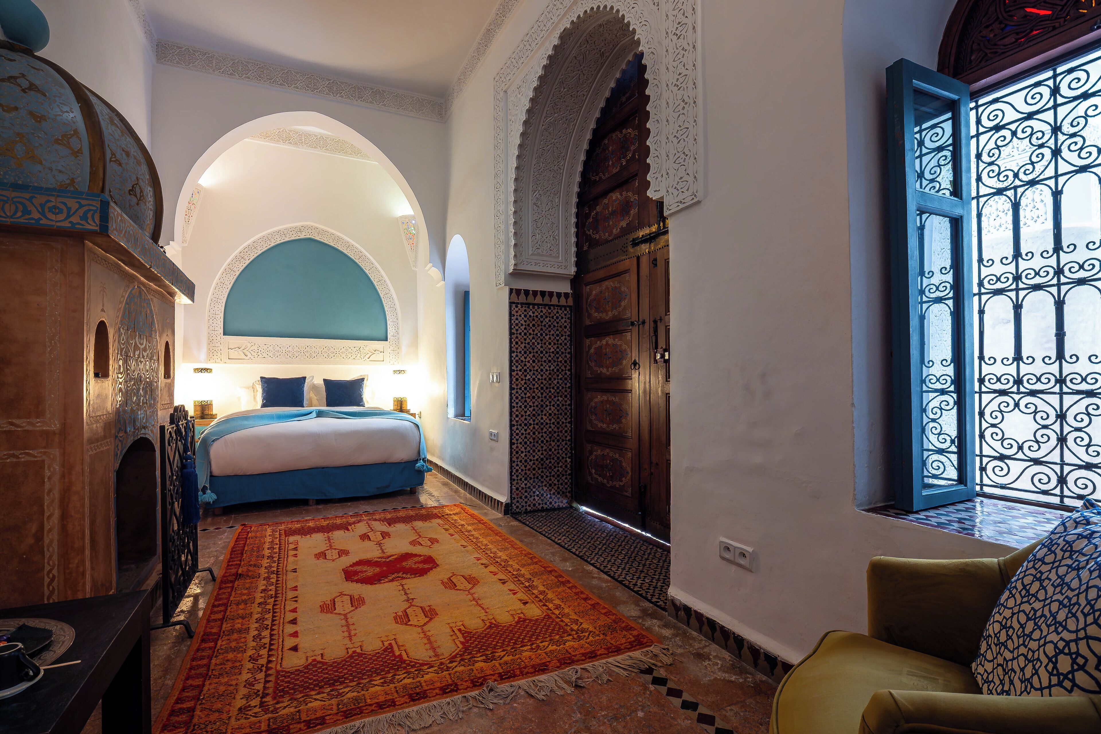 A room with a bed, a wooden cabinet, a patterned rug, and a window with decorative iron bars.