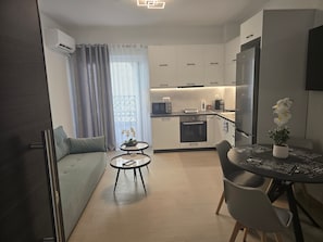 A modern kitchen with white cabinets, a built-in oven, and a microwave. There is a dining area with a round table and chairs, and a small round table with a plant.