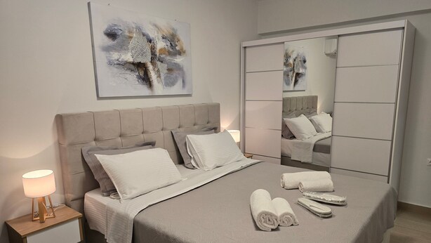 Ein modernes Schlafzimmer mit einem Bett, Nachttischen, einer Lampe, einem Spiegel und einem Gemälde an der Wand.