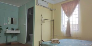 A bedroom with a bed, a window with curtains, a bedside table, a mirror, and an air conditioning unit. - Family suite 2 bedrooms for 6 pax (Hà Nội)