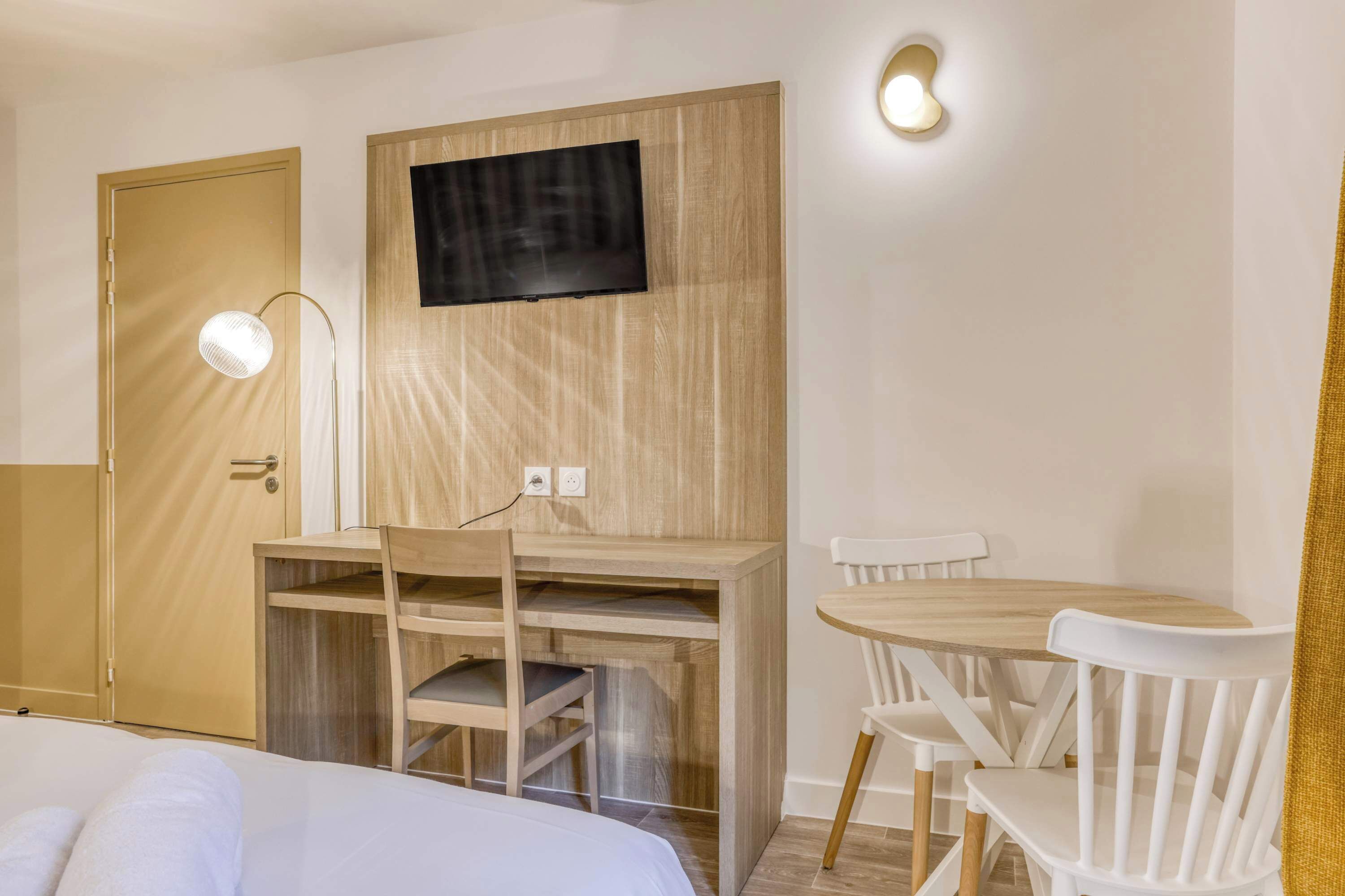 Hotelkamer met een bed, een bureau met stoel, een kleine tafel met stoelen, een aan de muur bevestigde televisie en een deur.