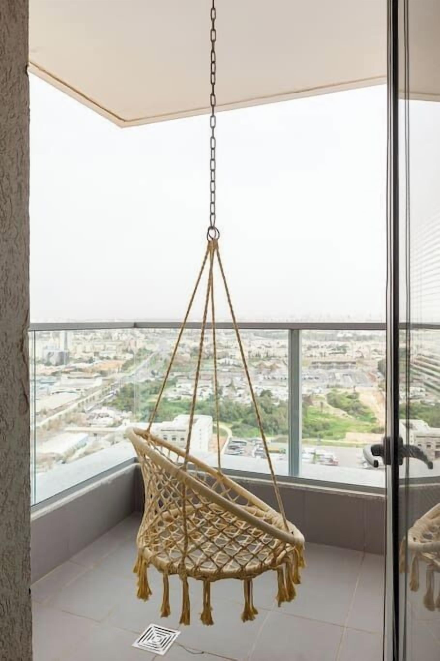 A macrame hanging chair in a balcony with a city view.