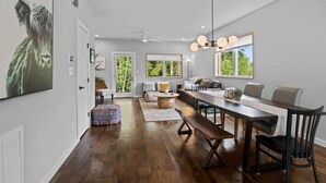 Amplia sala de estar con una mesa de comedor de madera, un sofá y un banco. Hay un ventanal con vistas a zonas verdes.