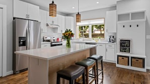 Una cocina moderna con armarios blancos, una isla central con taburetes, horno empotrado y un amplio ventanal con vistas al exterior.