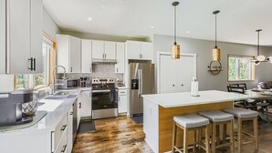 Cozinha moderna com armários brancos, eletrodomésticos de aço inoxidável e uma ilha central com banquetas.