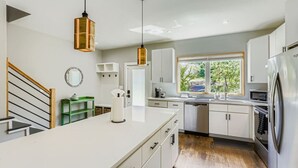 Cozinha moderna com armários brancos, geladeira de aço inoxidável e janela com vista para o verde lá fora.