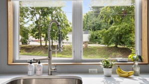 Eine Küche mit einem Edelstahl-Spülbecken, einem modernen Wasserhahn und einem Fenster mit Blick auf eine grüne Landschaft.