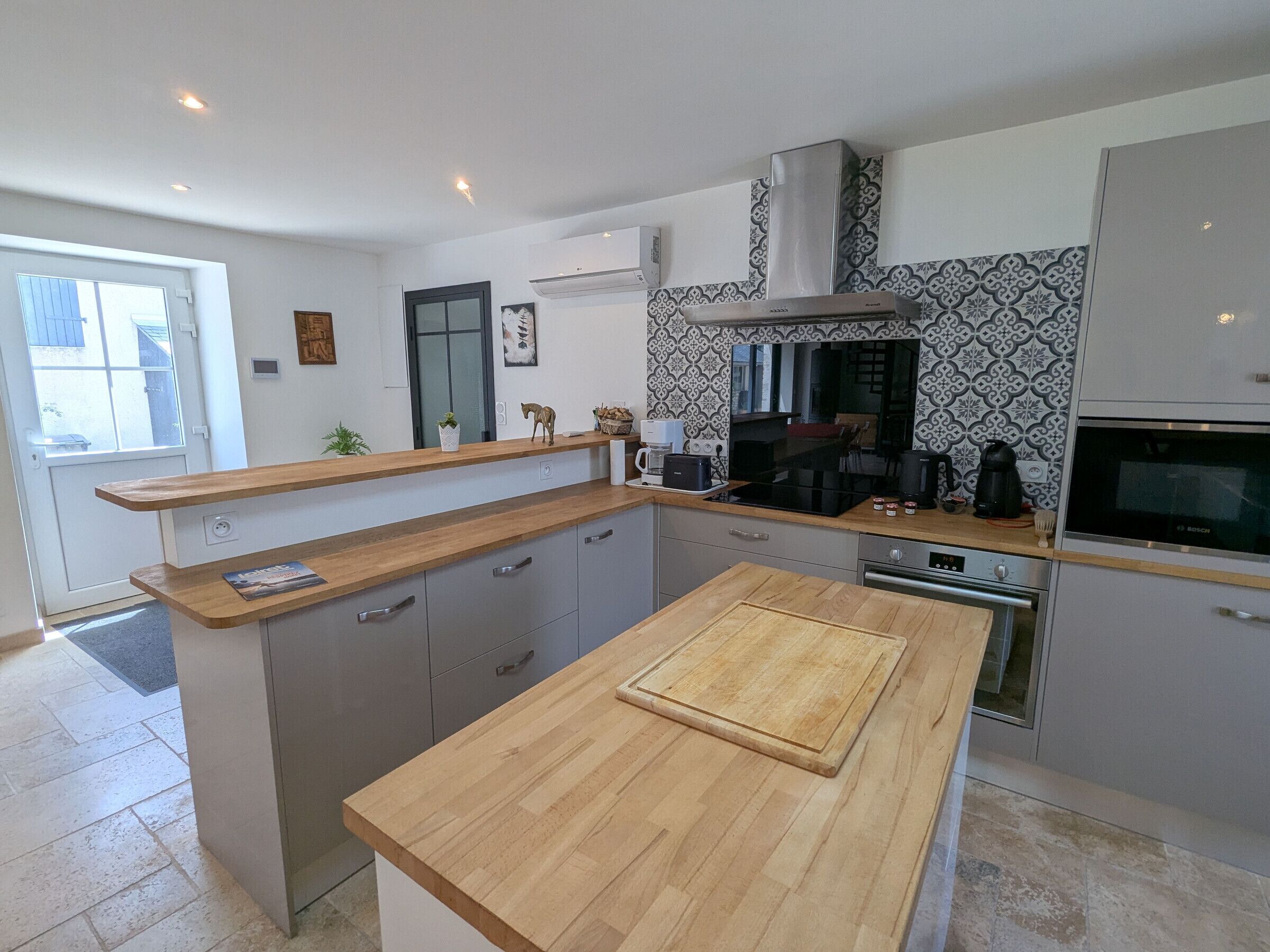 A modern kitchen with a central island, built-in appliances, and a patterned backsplash.