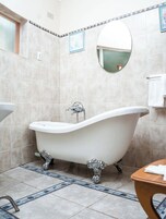 Un baño con una bañera independiente tipo patas de león, un espejo redondo y suelo de baldosas.