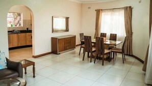 Uma área de refeições com mesa e cadeiras, um sofá, uma mesa de centro e uma cozinha ao fundo.