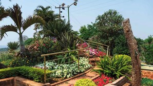 Um jardim com diversas plantas e flores, um caminho de tijolos e um corrimão de metal.