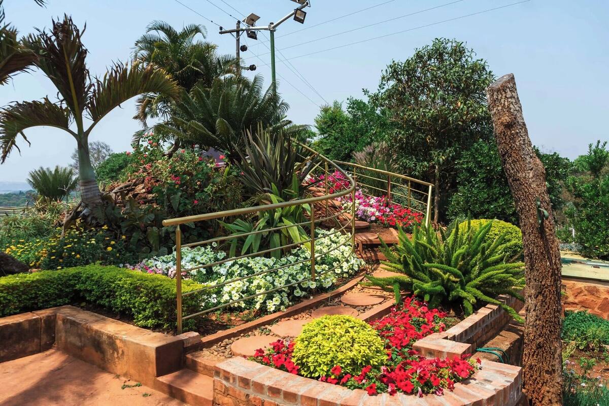 Un jardín con diversas plantas y flores, un camino de ladrillo y una barandilla de metal.