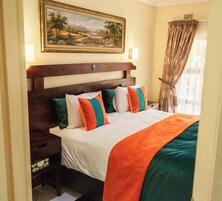 Habitación de hotel con una cama grande, cabecera de madera, un cuadro sobre la cama y una ventana con cortinas.
